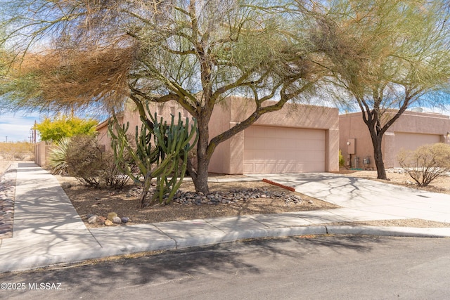 pueblo-style home with an attached garage, concrete driveway, and stucco siding