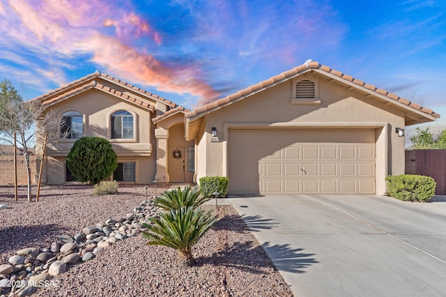 mediterranean / spanish home featuring concrete driveway, fence, an attached garage, and stucco siding