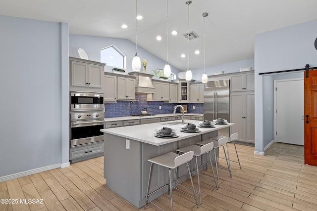 kitchen featuring a barn door, visible vents, built in appliances, premium range hood, and a sink