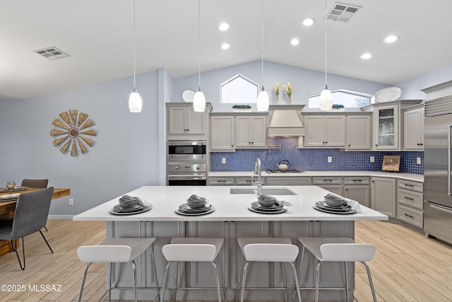 kitchen featuring built in appliances, visible vents, light wood finished floors, tasteful backsplash, and custom range hood