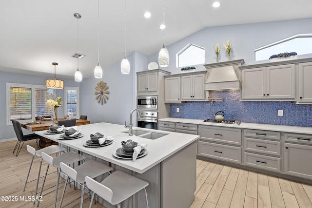 kitchen featuring stainless steel appliances, gray cabinetry, a sink, light wood-type flooring, and premium range hood