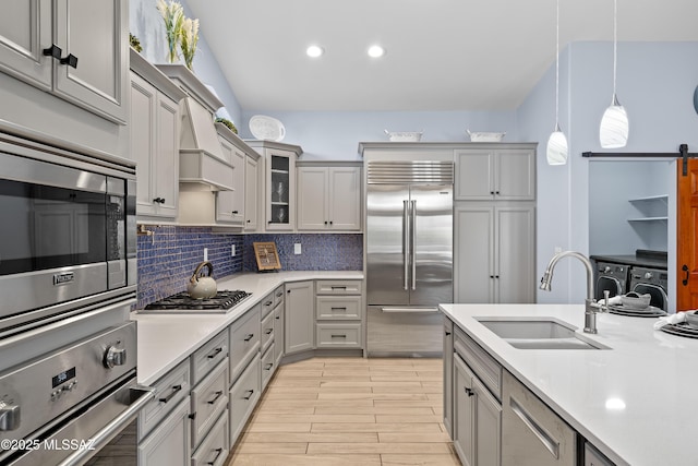 kitchen with decorative backsplash, decorative light fixtures, built in appliances, light countertops, and a sink