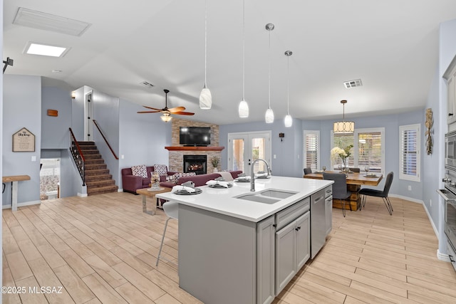 kitchen featuring gray cabinets, visible vents, appliances with stainless steel finishes, a sink, and a stone fireplace