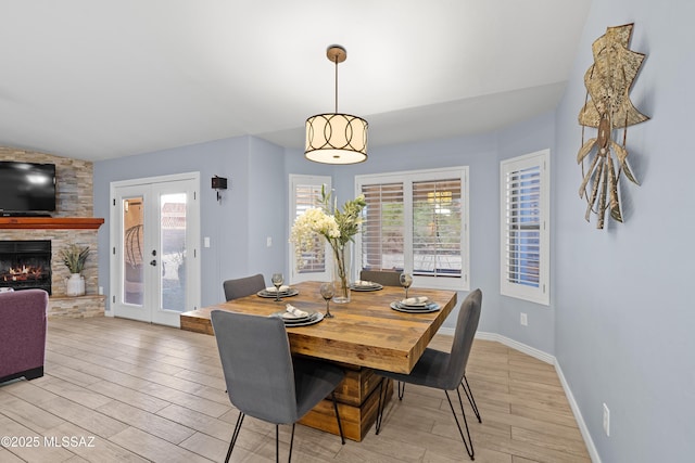 dining space with french doors, baseboards, a fireplace, and light wood finished floors