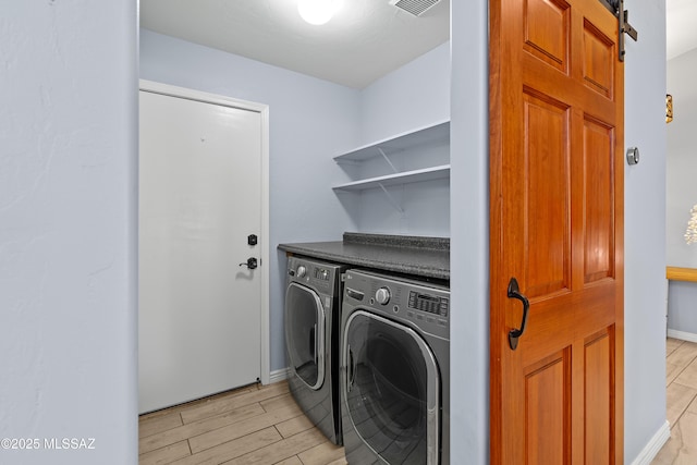 laundry room with washing machine and clothes dryer, visible vents, a barn door, wood tiled floor, and laundry area