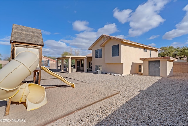 exterior space featuring a tile roof, an outbuilding, fence, a playground, and stucco siding