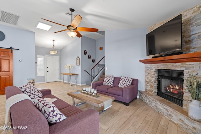 living room featuring a fireplace, visible vents, a barn door, light wood-style floors, and a ceiling fan