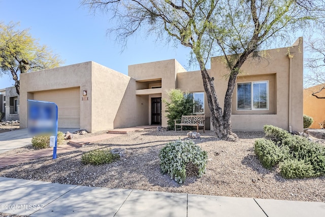 pueblo revival-style home featuring driveway, an attached garage, and stucco siding