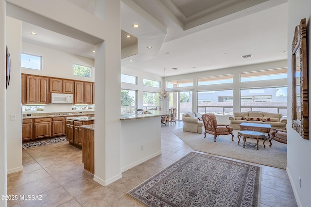 kitchen with brown cabinetry, a wealth of natural light, a towering ceiling, and white microwave