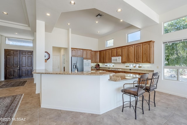 kitchen with stainless steel fridge, visible vents, white microwave, a high ceiling, and a healthy amount of sunlight