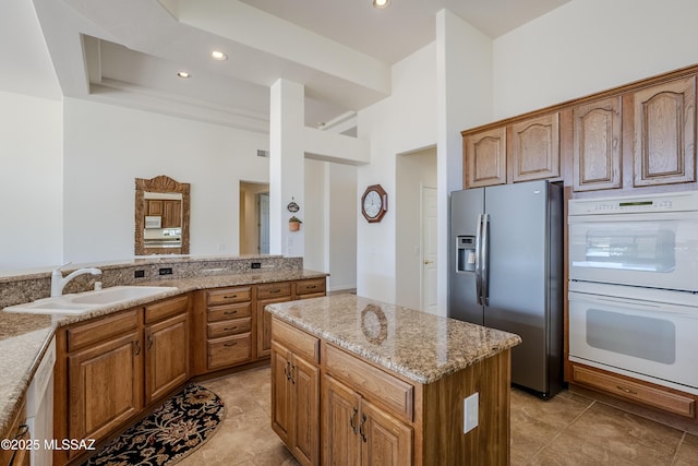 kitchen with double oven, a sink, light stone countertops, dishwasher, and stainless steel fridge with ice dispenser