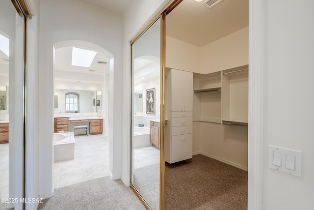 walk in closet featuring visible vents, arched walkways, and light colored carpet