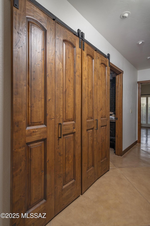 hall with a barn door, baseboards, and finished concrete flooring