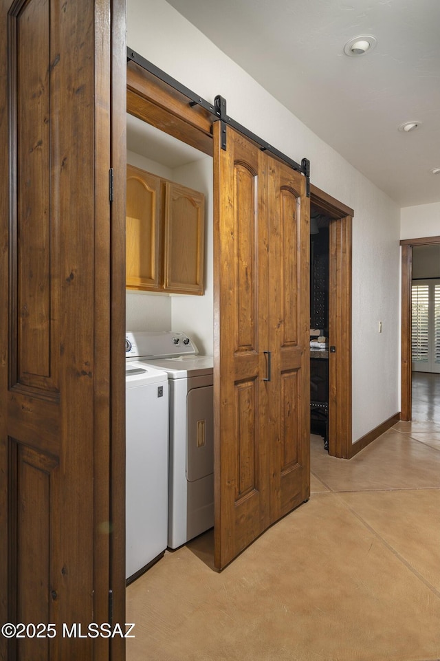 washroom featuring cabinet space, washing machine and dryer, baseboards, and a barn door