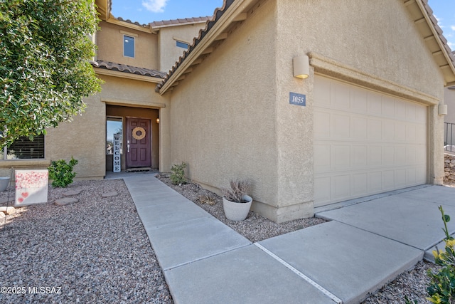 entrance to property with an attached garage, a tile roof, and stucco siding