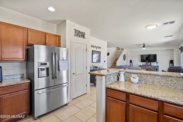 kitchen with light stone counters, brown cabinets, visible vents, open floor plan, and stainless steel fridge