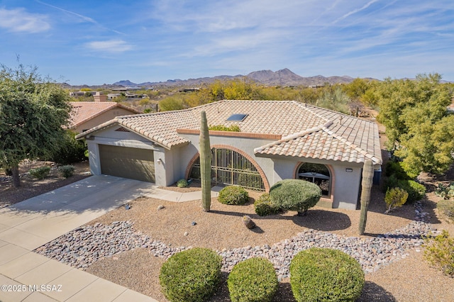 mediterranean / spanish-style home with concrete driveway, a tiled roof, an attached garage, a mountain view, and stucco siding