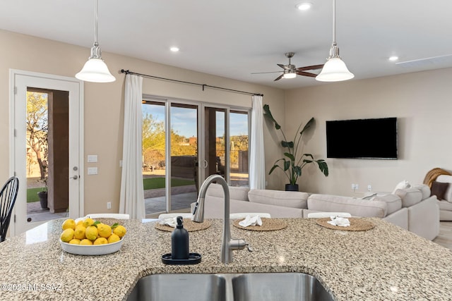 kitchen featuring light stone counters, sink, pendant lighting, and ceiling fan