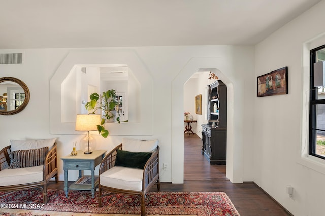 sitting room featuring dark wood-style floors, arched walkways, and visible vents