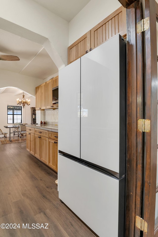 kitchen with arched walkways, dark wood-style flooring, freestanding refrigerator, light brown cabinetry, and backsplash