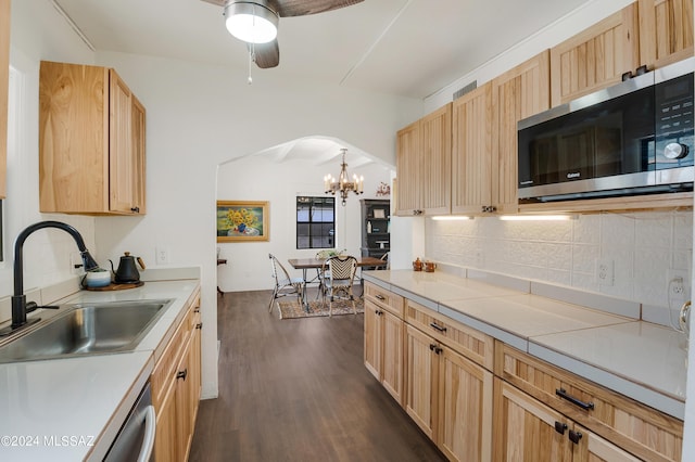 kitchen with arched walkways, dark wood-type flooring, a sink, tasteful backsplash, and stainless steel microwave