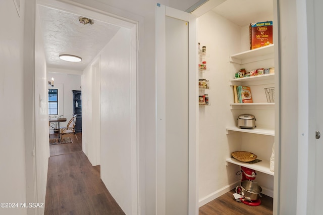 hall featuring a textured ceiling, dark wood-type flooring, and baseboards