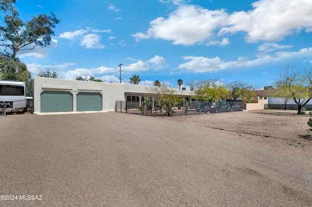 pueblo-style house with driveway, an attached garage, fence, and stucco siding