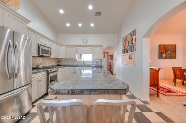 kitchen with visible vents, a kitchen island, recessed lighting, stainless steel appliances, and arched walkways