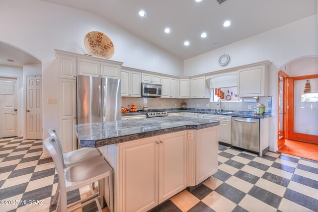 kitchen with light floors, arched walkways, appliances with stainless steel finishes, and a center island