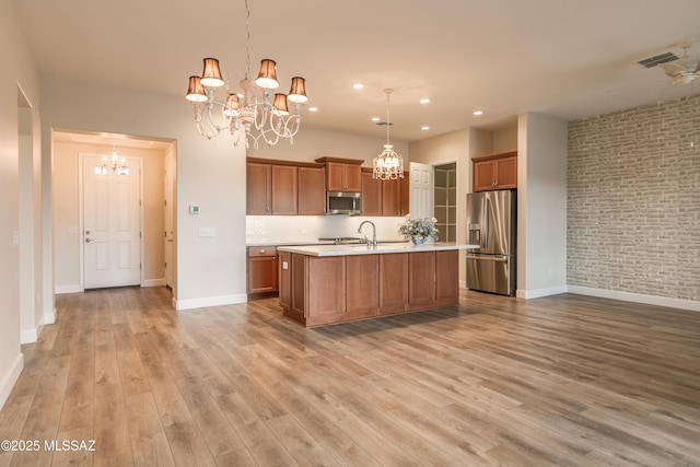 kitchen featuring stainless steel appliances, a kitchen island with sink, a notable chandelier, and decorative light fixtures