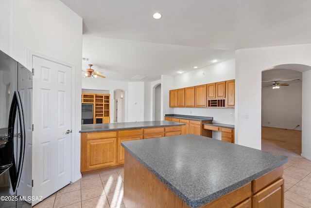 kitchen with black fridge with ice dispenser, light tile patterned flooring, ceiling fan, and a kitchen island