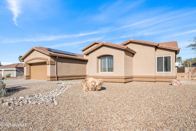 view of front facade featuring roof mounted solar panels, driveway, a tiled roof, and stucco siding