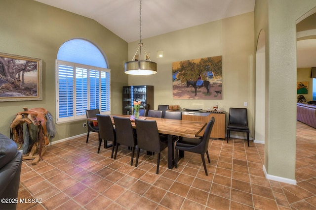 tiled dining room featuring lofted ceiling, baseboards, and arched walkways