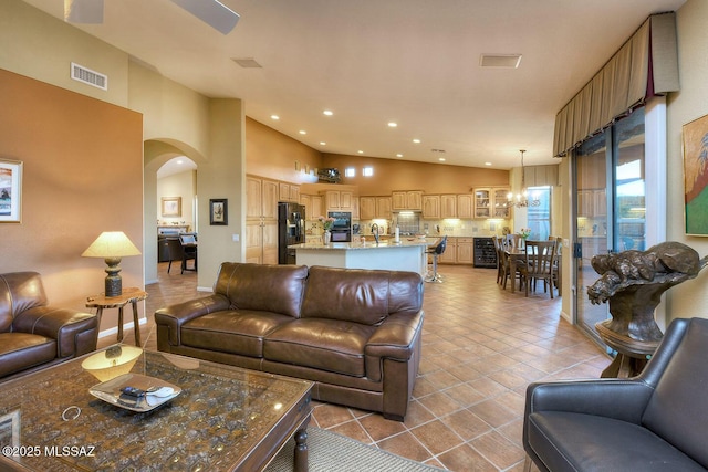 tiled living room featuring arched walkways, recessed lighting, visible vents, an inviting chandelier, and high vaulted ceiling