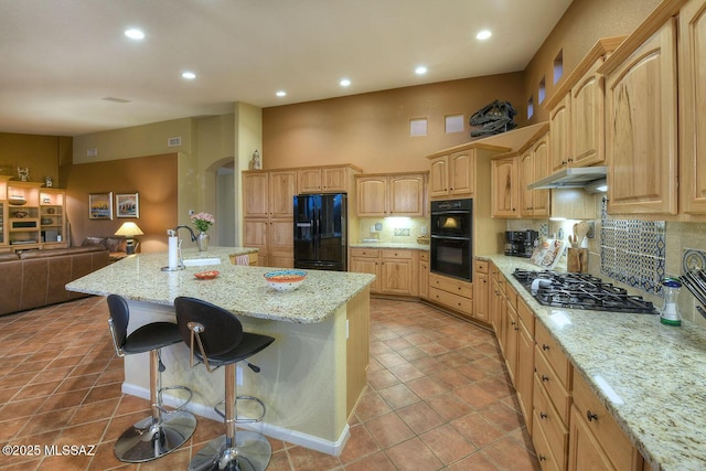 kitchen featuring under cabinet range hood, open floor plan, light brown cabinetry, decorative backsplash, and black appliances