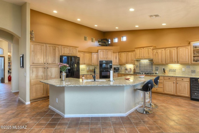 kitchen featuring arched walkways, light brown cabinets, a spacious island, visible vents, and black appliances