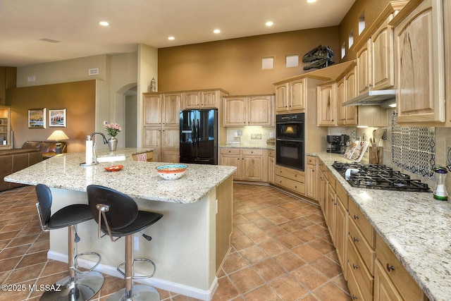 kitchen with a kitchen breakfast bar, backsplash, black appliances, and light brown cabinetry