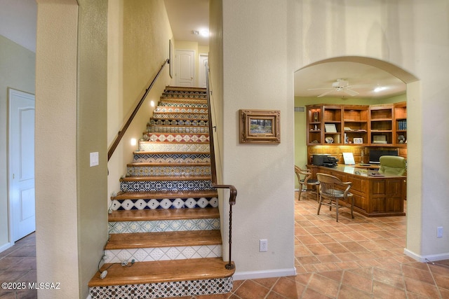 stairway featuring arched walkways, ceiling fan, tile patterned flooring, and baseboards