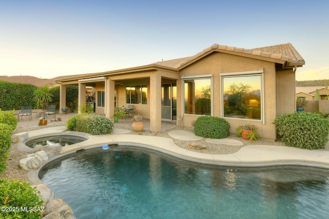 back of house featuring an in ground hot tub, a patio area, a tiled roof, and stucco siding