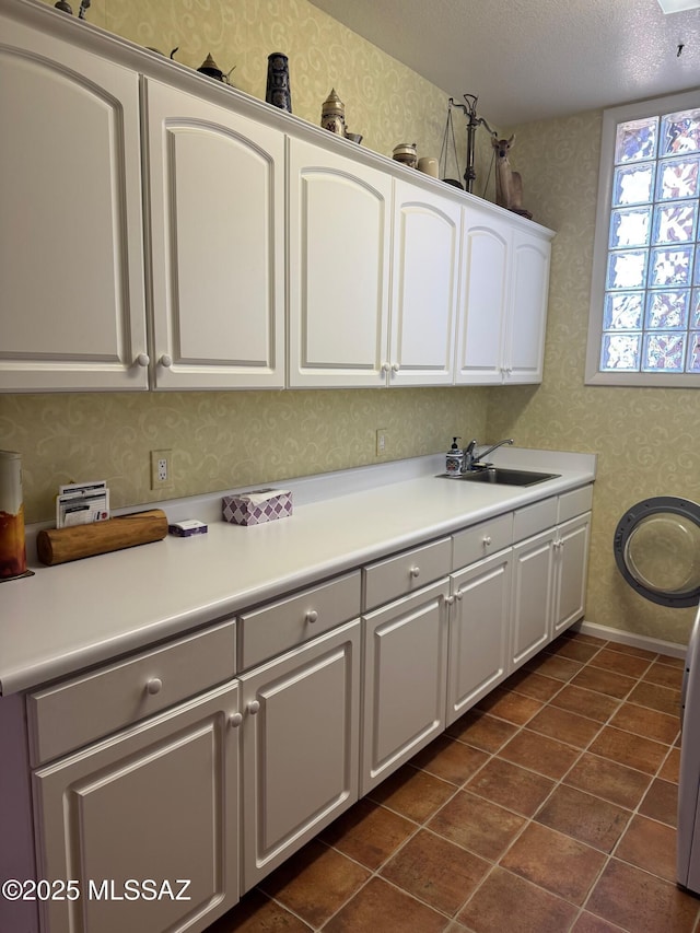 kitchen with light countertops, a sink, white cabinets, and wallpapered walls