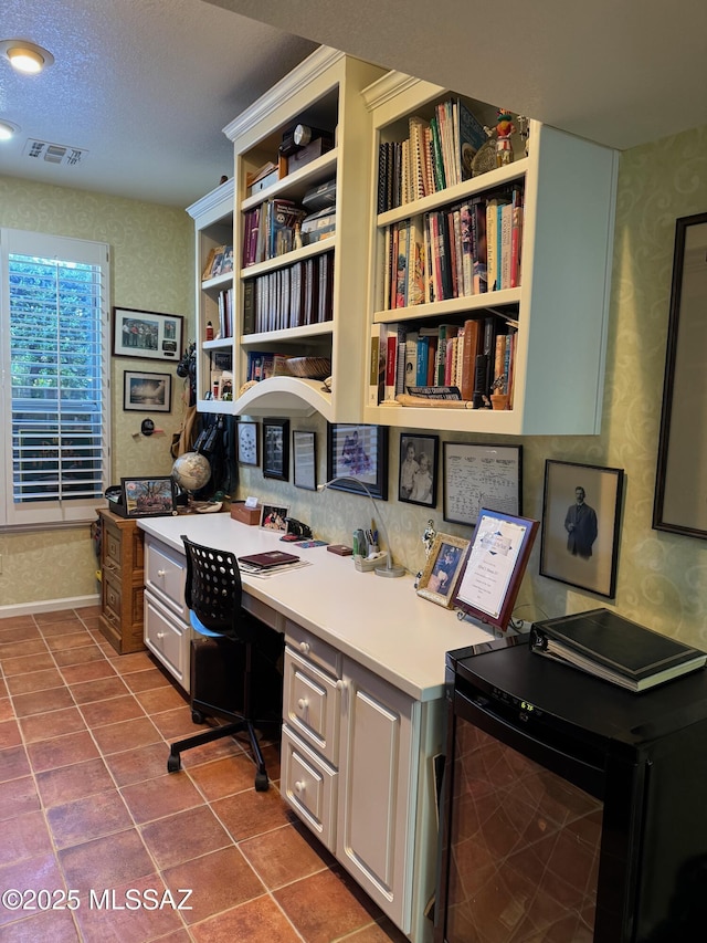 office featuring a textured ceiling, dark tile patterned flooring, visible vents, built in desk, and wallpapered walls