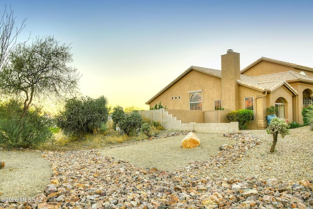 view of home's exterior featuring a tile roof, a chimney, and stucco siding