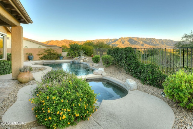 view of swimming pool featuring a fenced backyard, a mountain view, a fenced in pool, and an in ground hot tub