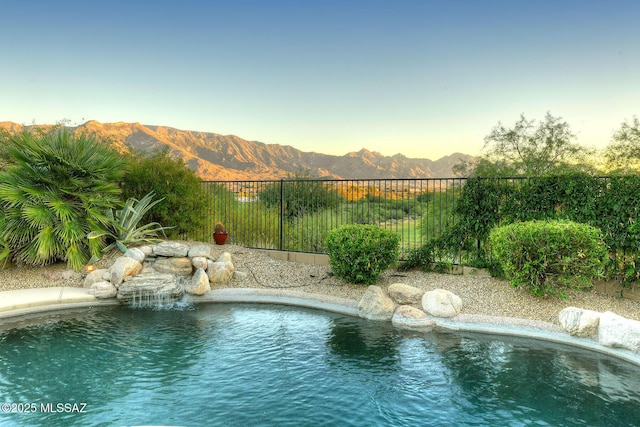 view of swimming pool with fence and a mountain view