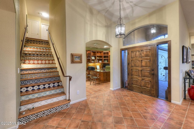 foyer featuring a towering ceiling, tile patterned flooring, arched walkways, and baseboards