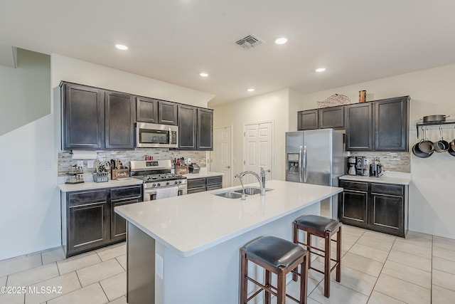 kitchen with sink, a kitchen bar, light tile patterned floors, stainless steel appliances, and a center island with sink