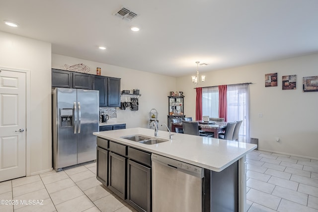 kitchen with light tile patterned flooring, sink, hanging light fixtures, stainless steel appliances, and a kitchen island with sink