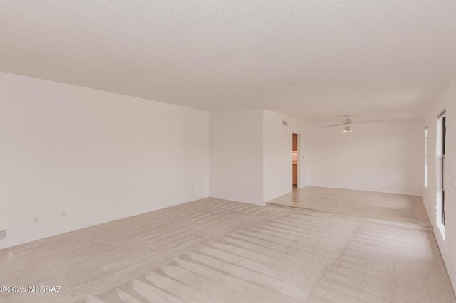 empty room with a textured ceiling, ceiling fan, and light colored carpet