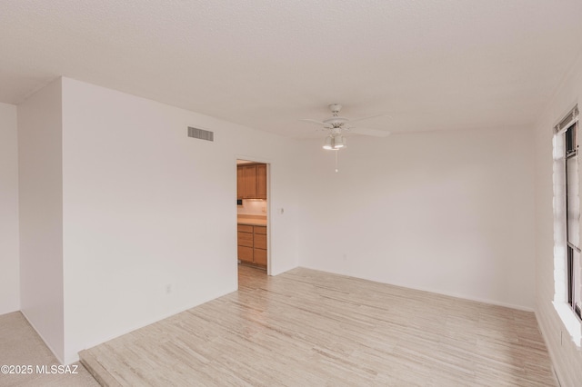 empty room featuring ceiling fan, light wood-type flooring, and visible vents