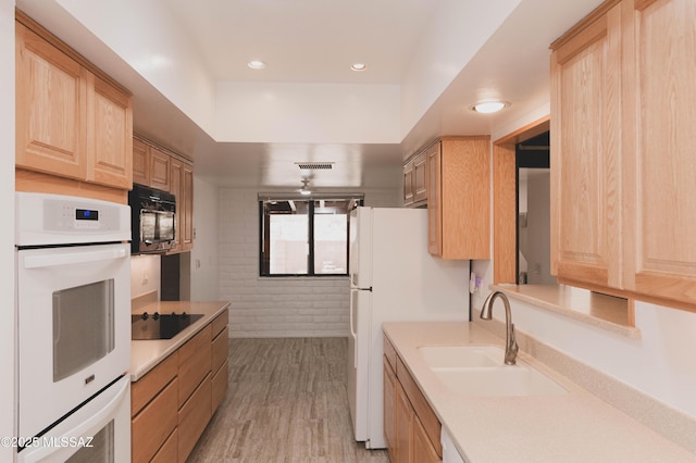 kitchen featuring light countertops, light brown cabinets, a sink, and black appliances